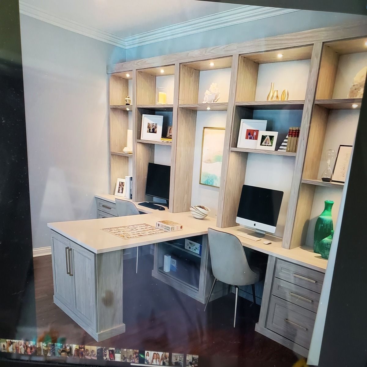 Built-in light wood home office with a desk, shelving, two computer monitors, and decorative items.