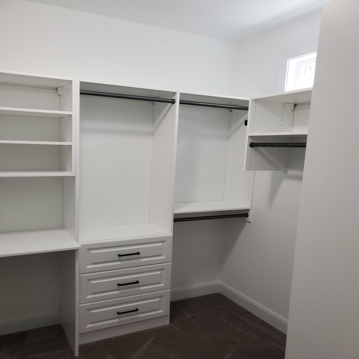 White custom closet organization system with shelving, drawers, and hanging rods in a room with neutral carpet.