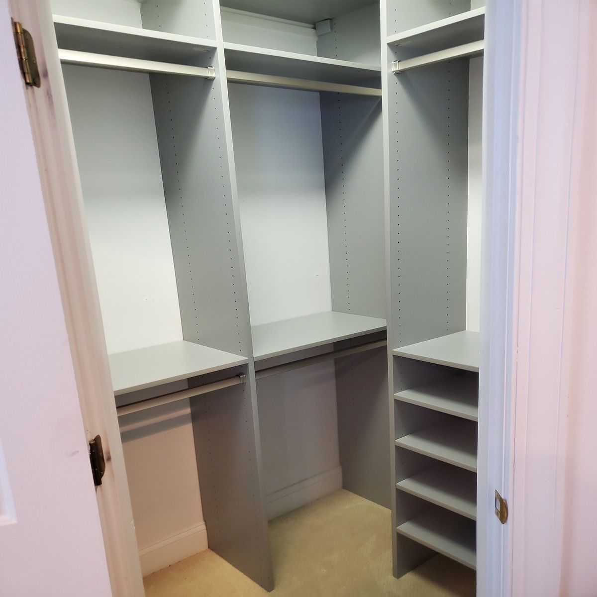 Empty gray closet with shelves and hanging rods in a bedroom. Doorway on left and right.