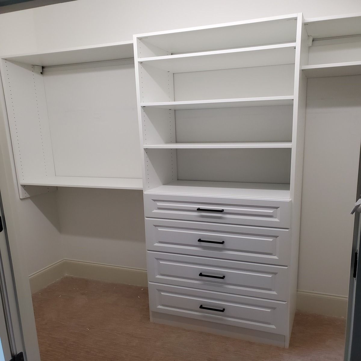 A white custom closet system with drawers and shelves, empty, set against a beige carpet.