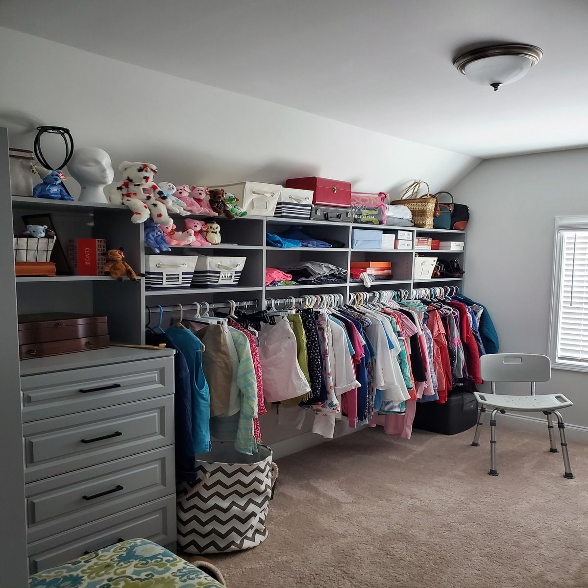 Walk-in closet with gray shelves and clothes hanging on rods, a dresser, and a gray chair.