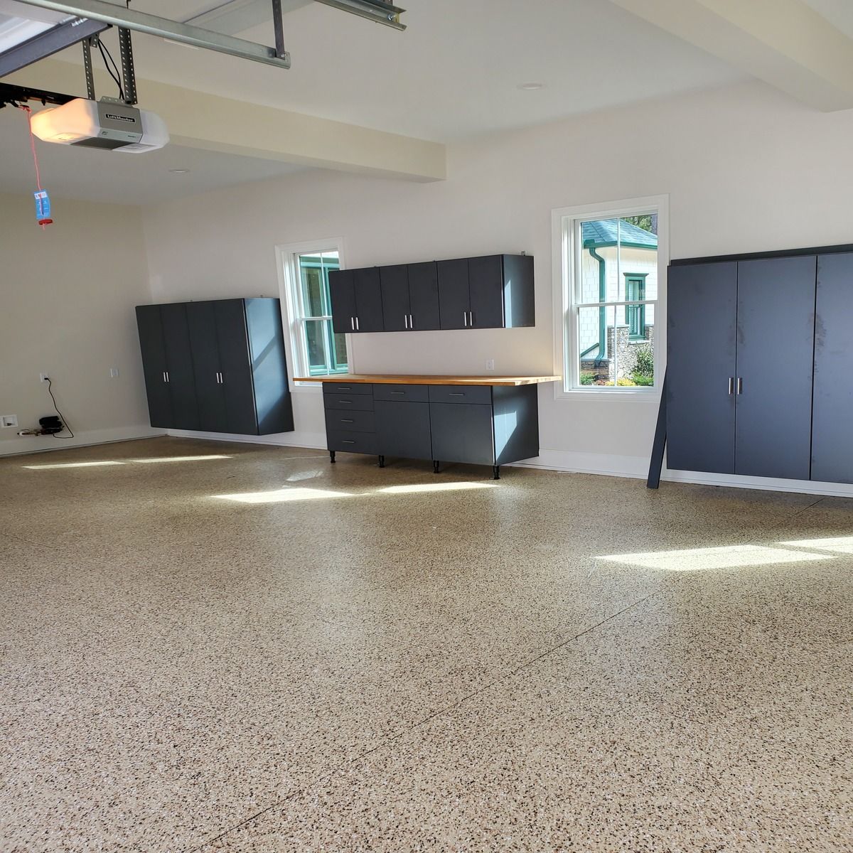 A clean garage with grey cabinets and a speckled floor. Sunlight streams through the windows.