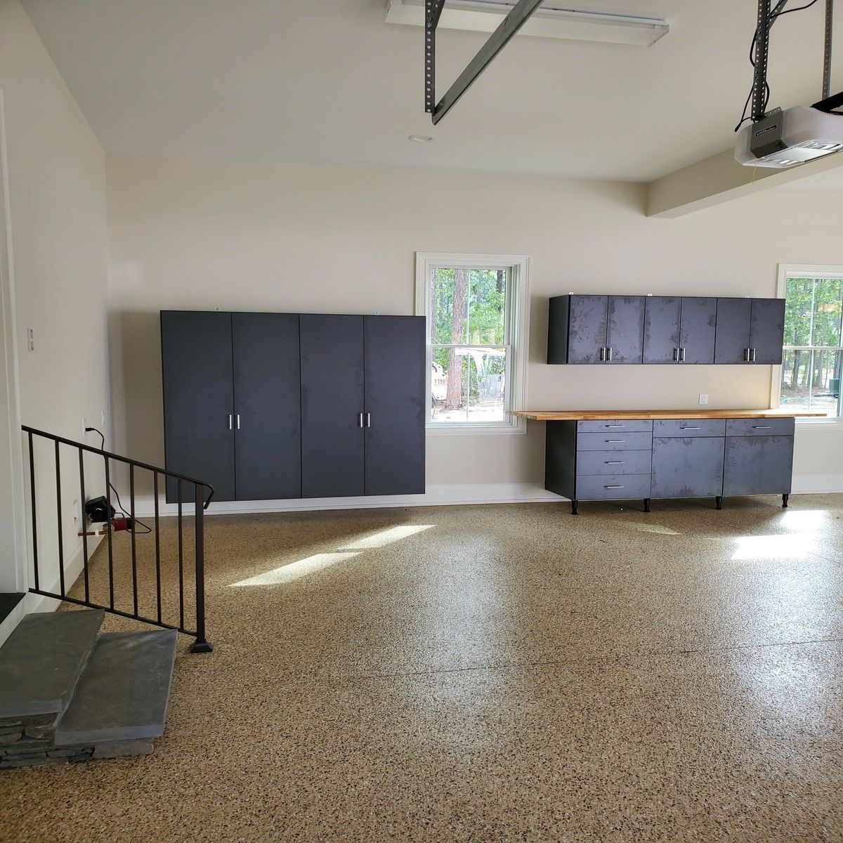 Garage with dark gray cabinets, a work bench, and epoxy flooring. A small staircase leads up to the garage.