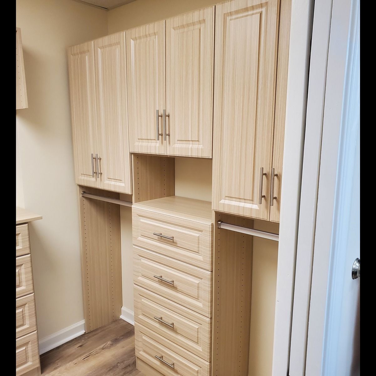 Light wood closet organization system with upper cabinets, drawers, and hanging rods.