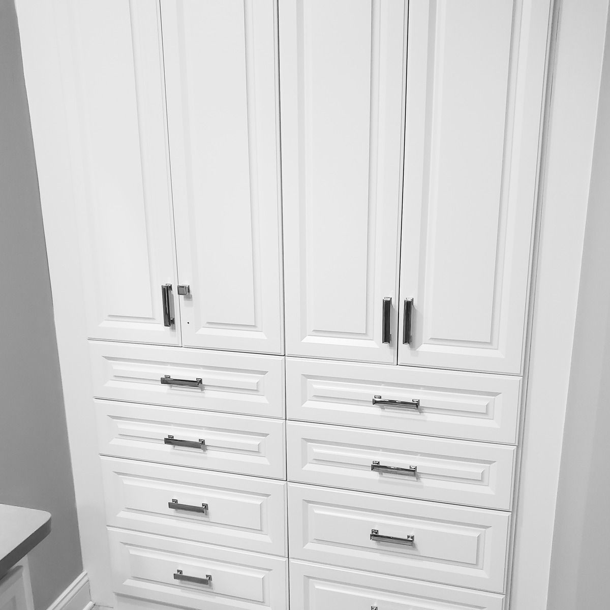 White built-in cabinet with doors and drawers. Black handles provide contrast against the white.