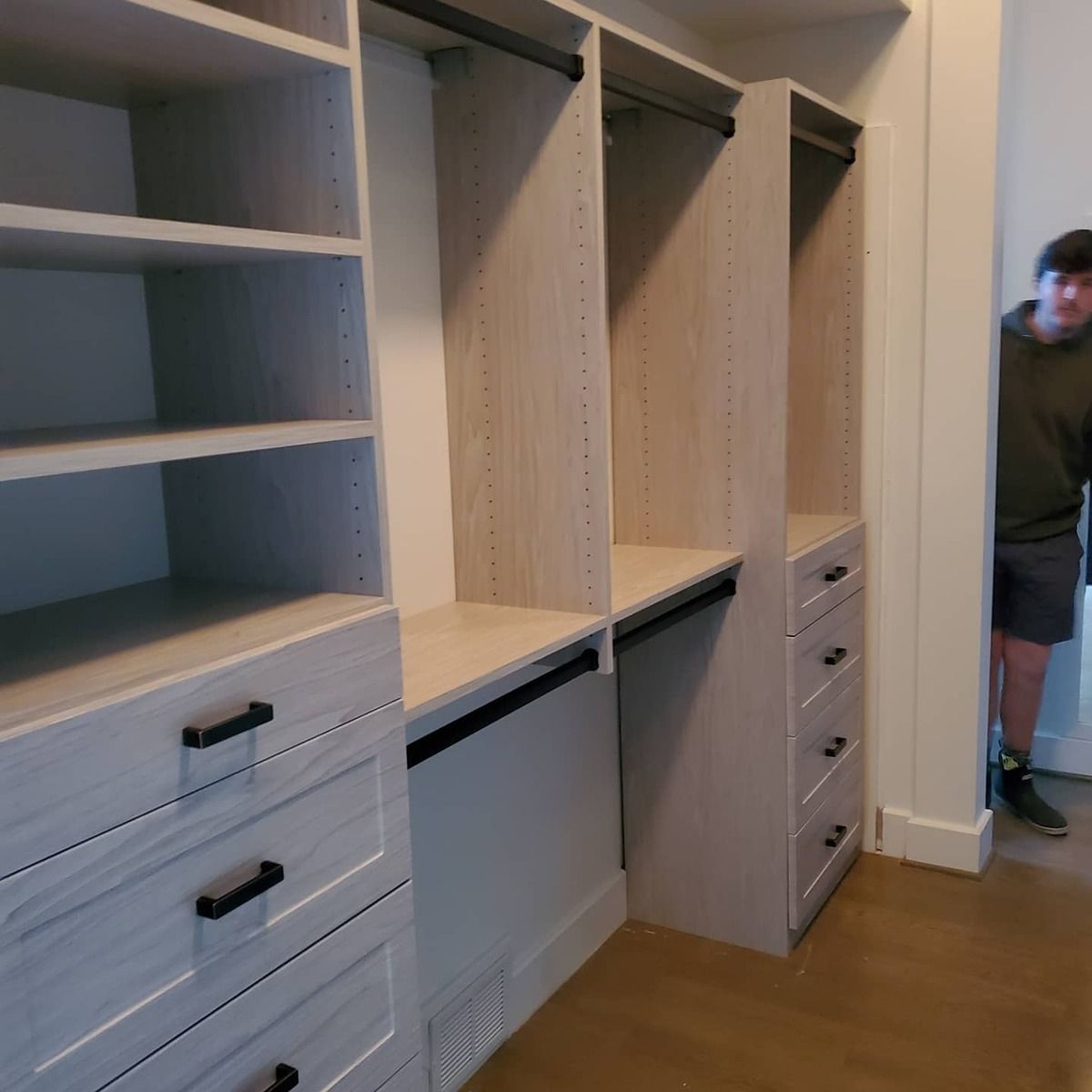 A custom walk-in closet with shelving, drawers, and hanging rods. A person peeks from the doorway.