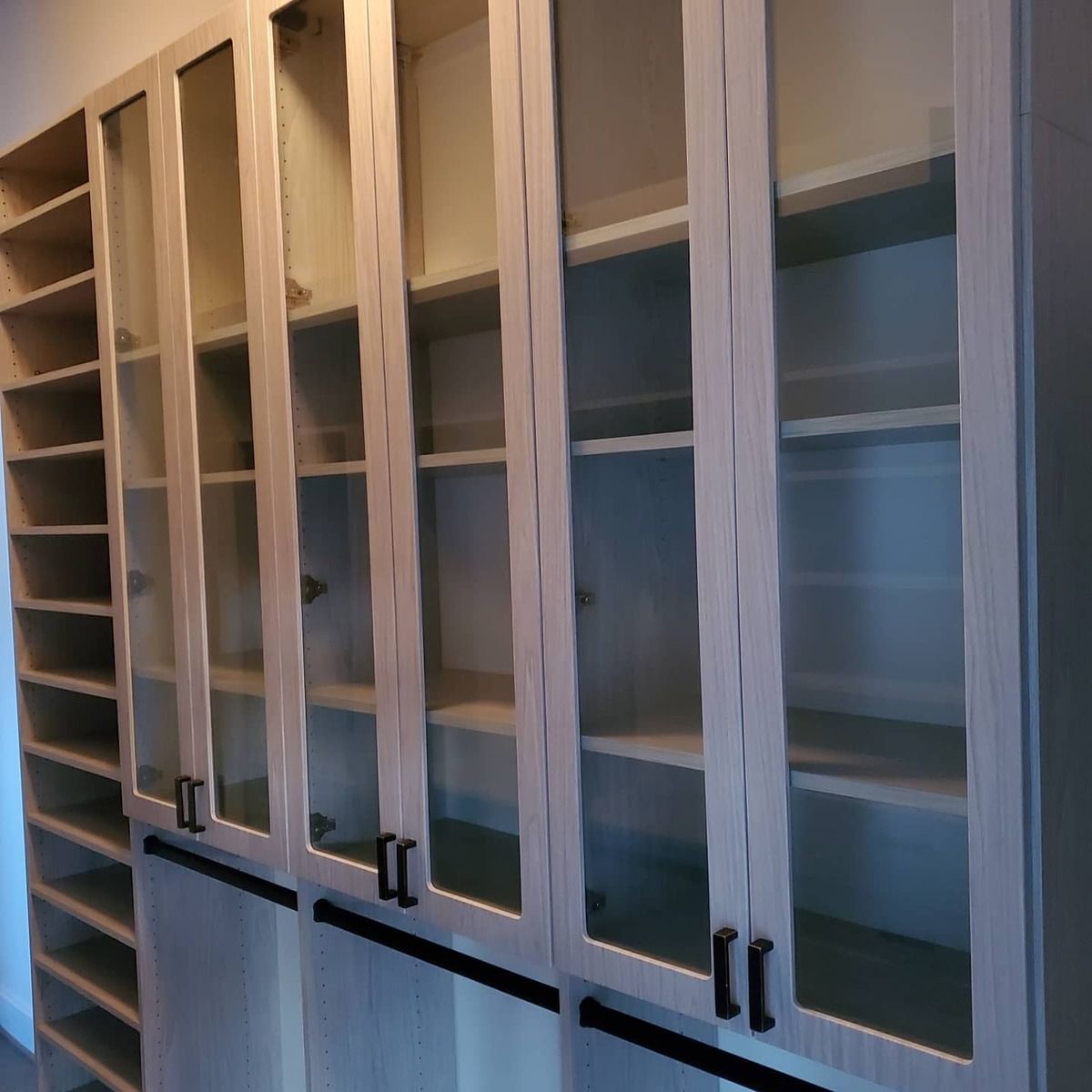 Light-colored built-in cabinet with glass-front doors. The shelves are empty, and there are black handles on the doors.