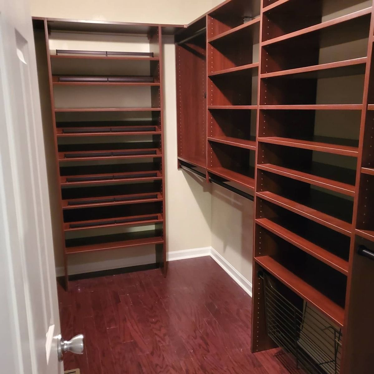 Walk-in closet with dark wood shelving. Shelves line the walls, and a hanging rod is visible. Dark wood flooring.