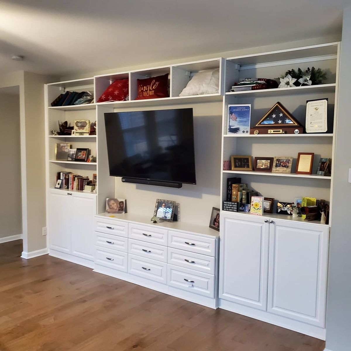 Built-in white entertainment center with a mounted TV and shelves displaying decor in a living room with hardwood floors.