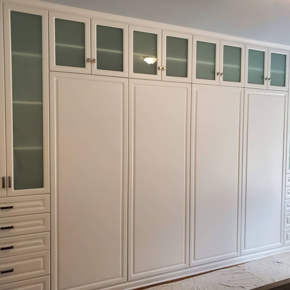 White built-in closet with drawers, solid cabinet doors, and glass-door upper cabinets. Located against a wall.