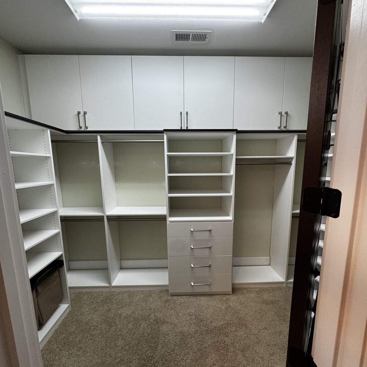 An organized, white-walled closet with built-in shelves, drawers, and hanging rods. The closet is empty, showcasing its storage design.