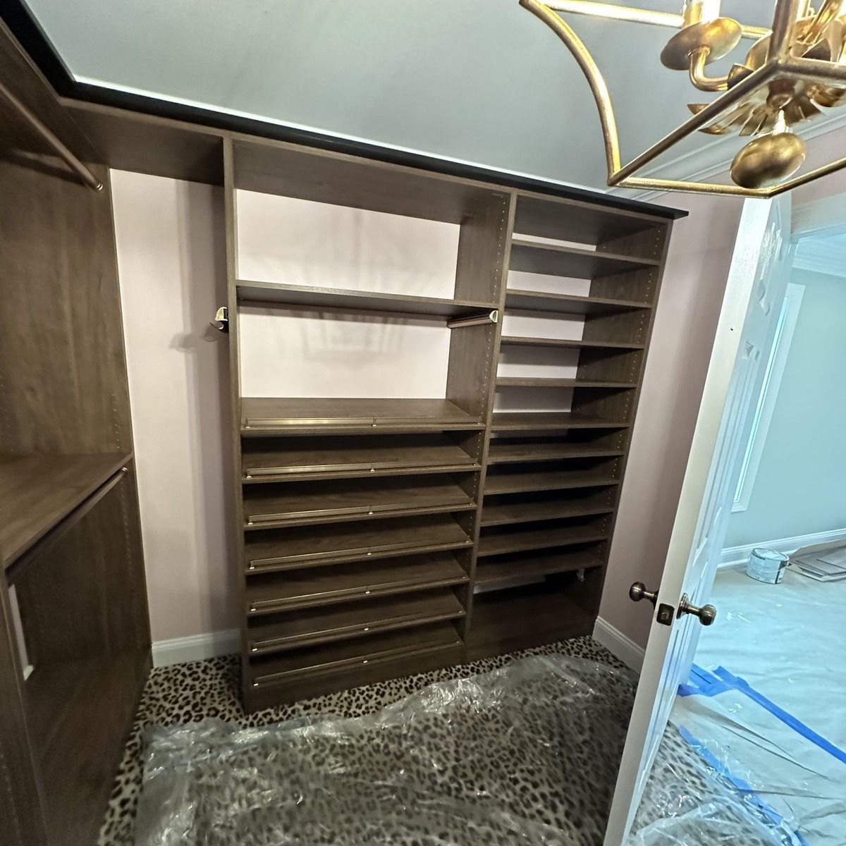 Built-in closet with shelves and shoe storage, brown wood finish, against a pink wall, leopard print floor.