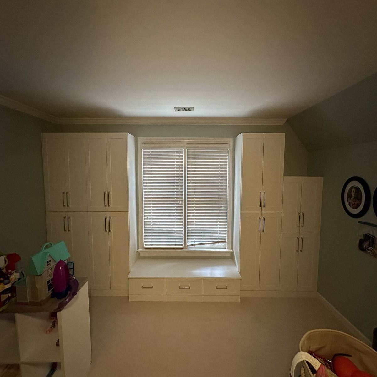 Bedroom with window seat flanked by white storage cabinets, with a window featuring blinds.