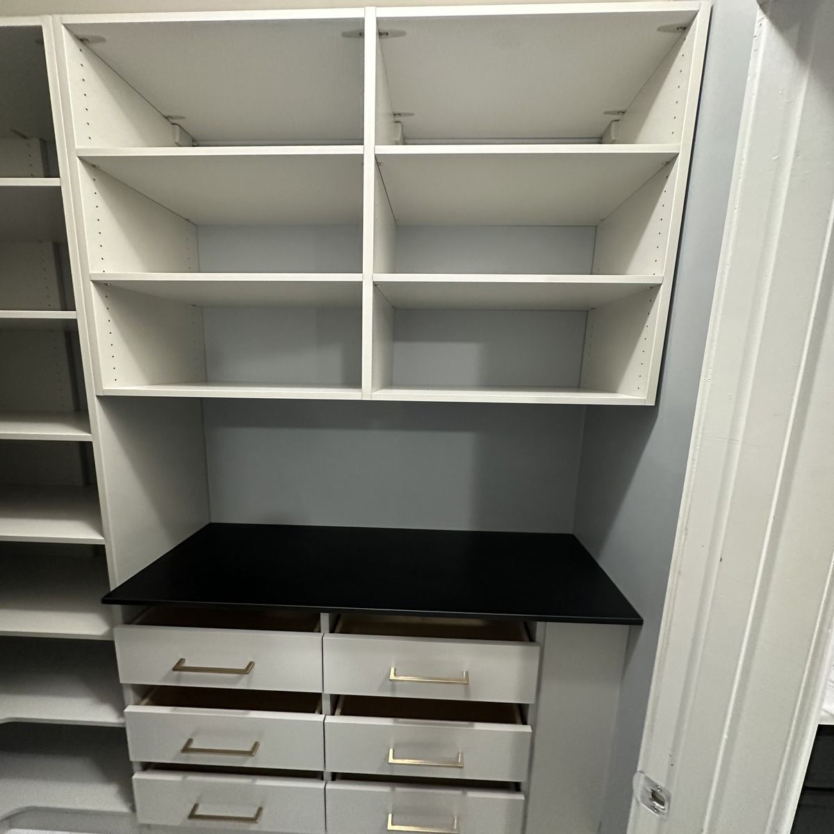 White closet shelves above a black countertop with six drawers. The drawers have gold handles.