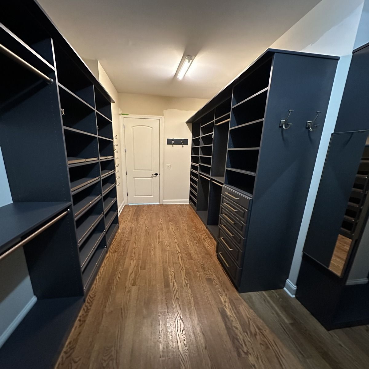Walk-in closet with dark blue shelving and hardwood floors. A door is at the end of the hall.