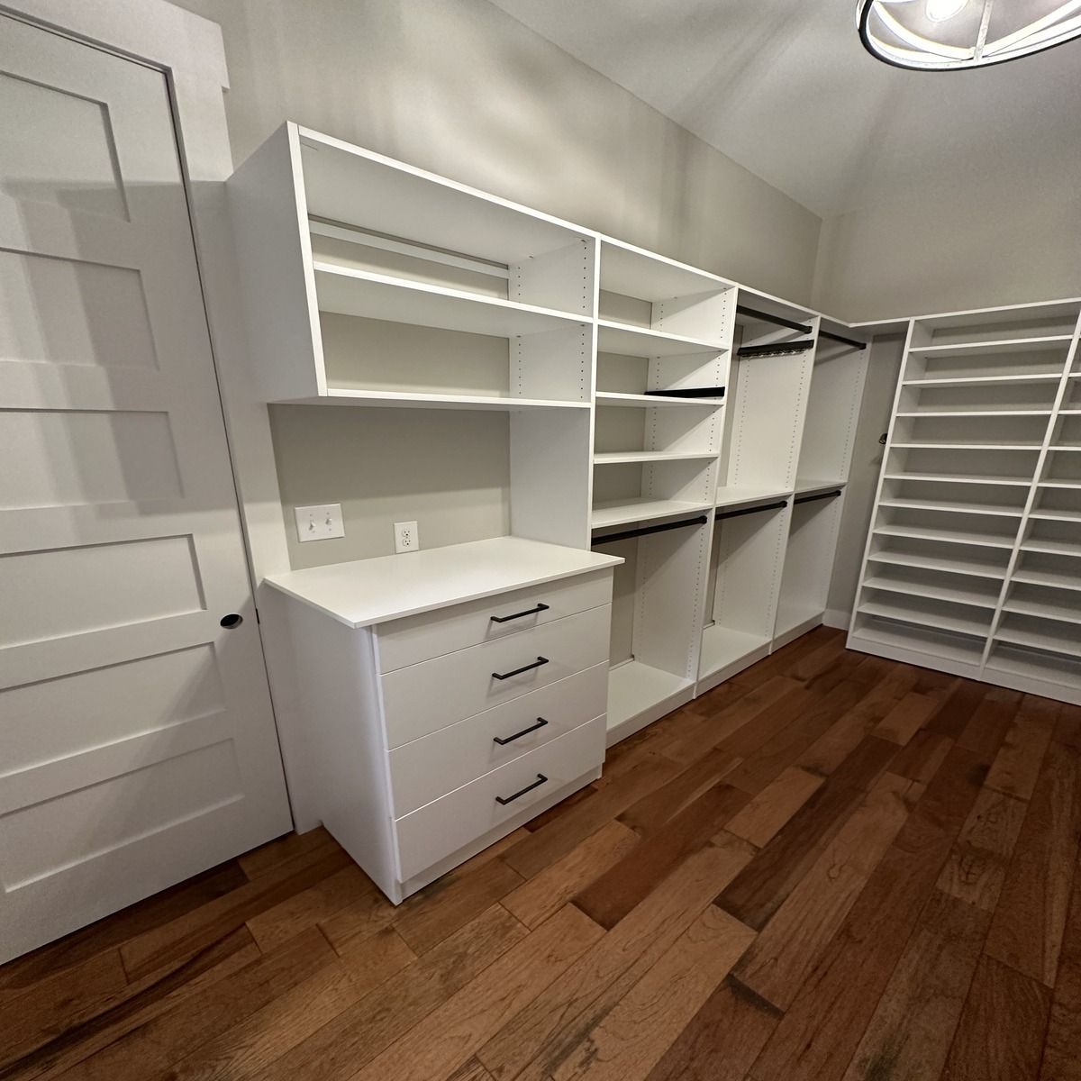White custom closet shelving with drawers and hanging rods, set in a room with hardwood floors.