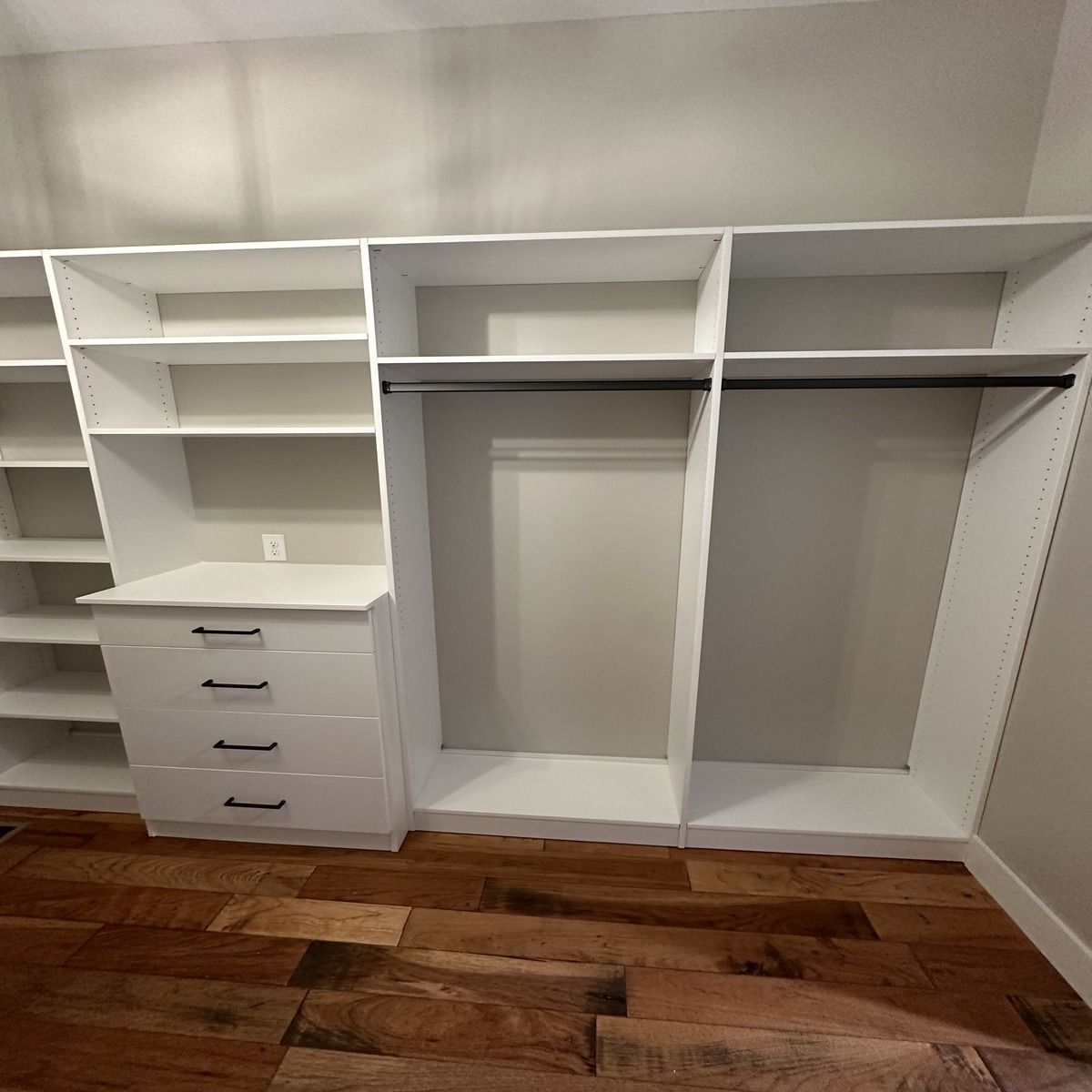 White custom closet with shelves, drawers, and hanging rod against a neutral wall, on a hardwood floor.
