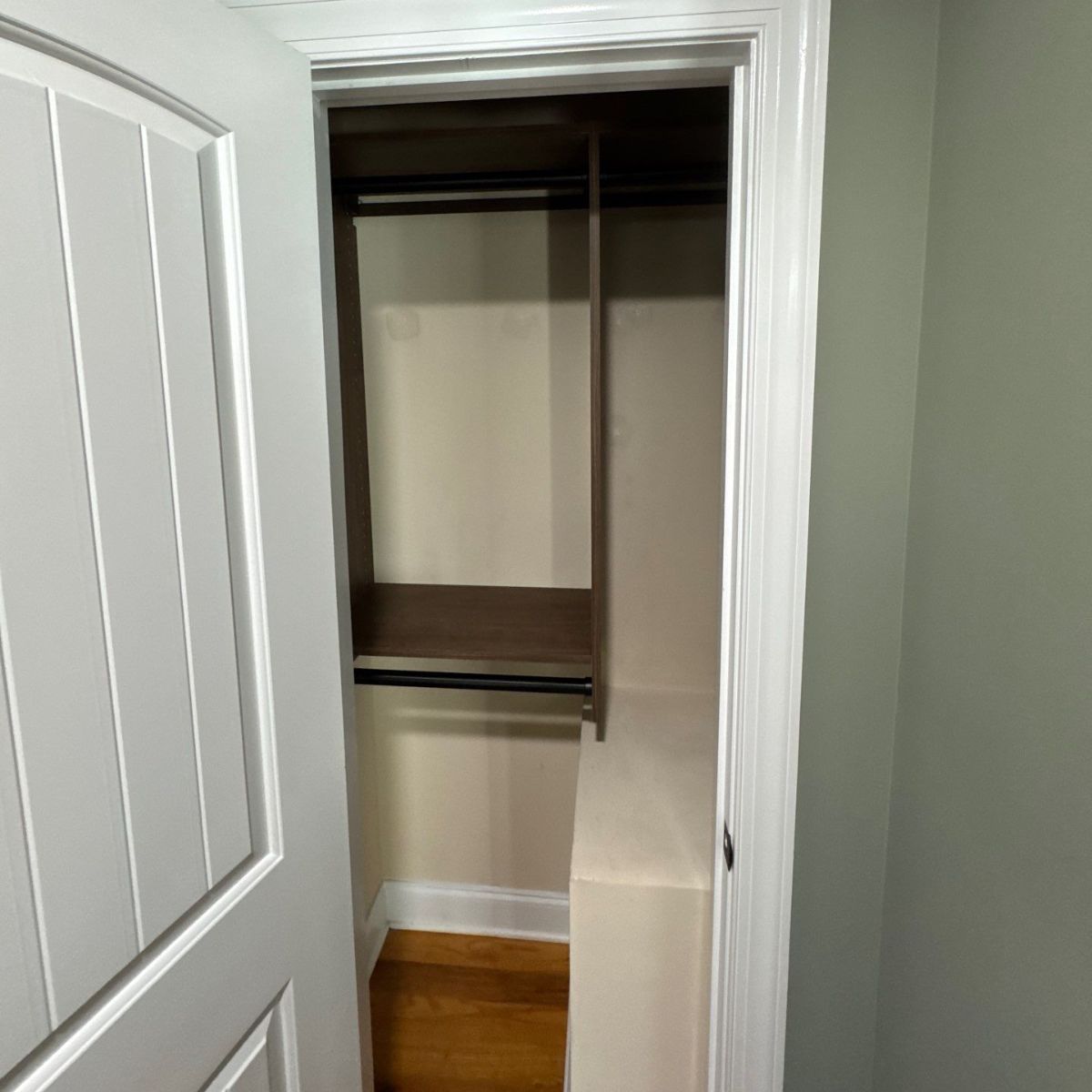 Open closet with a shelf and hanging rods. The door is white, and the walls are a light green.