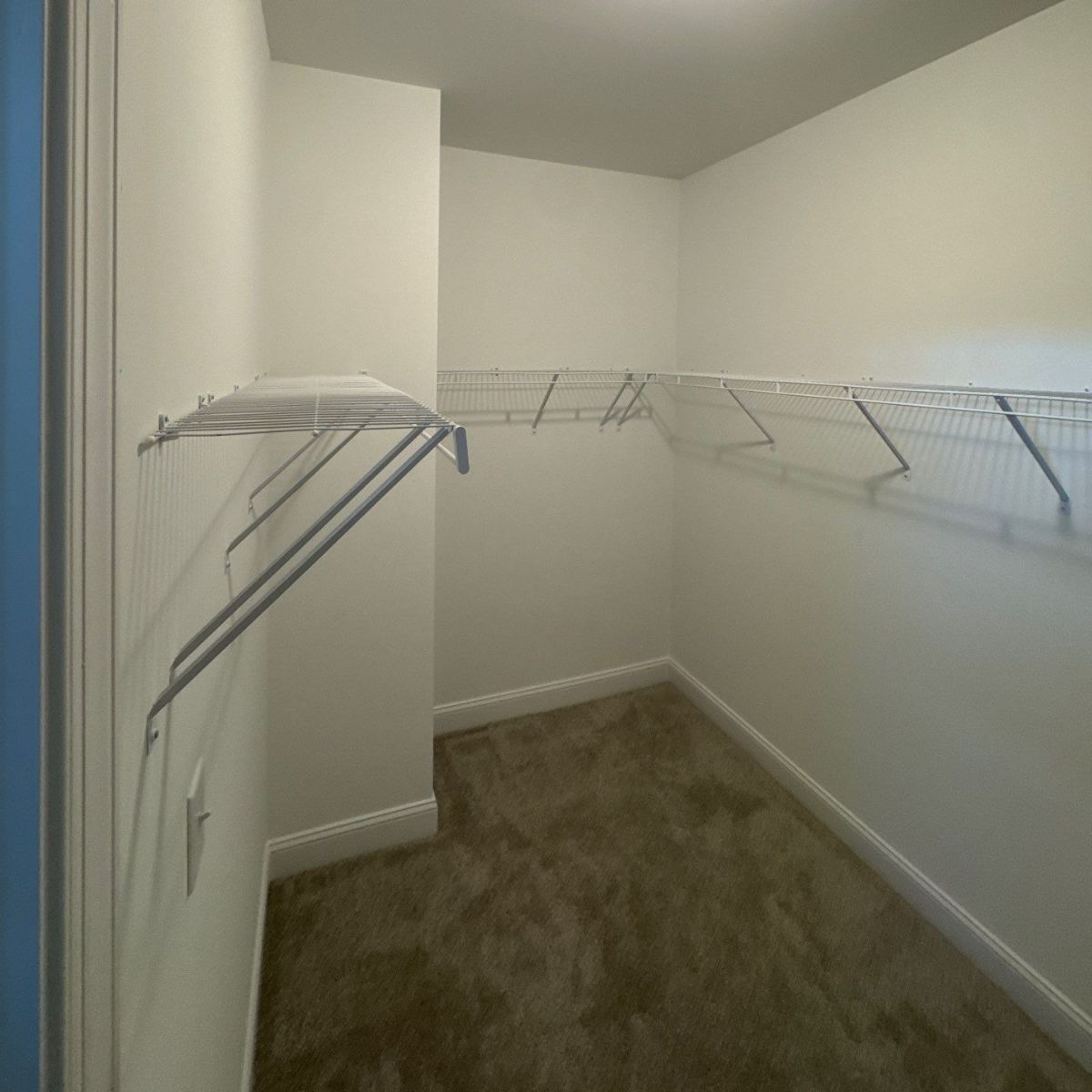 Empty walk-in closet with wire shelving. White walls and trim, carpeted floor, and an open doorway on the left.