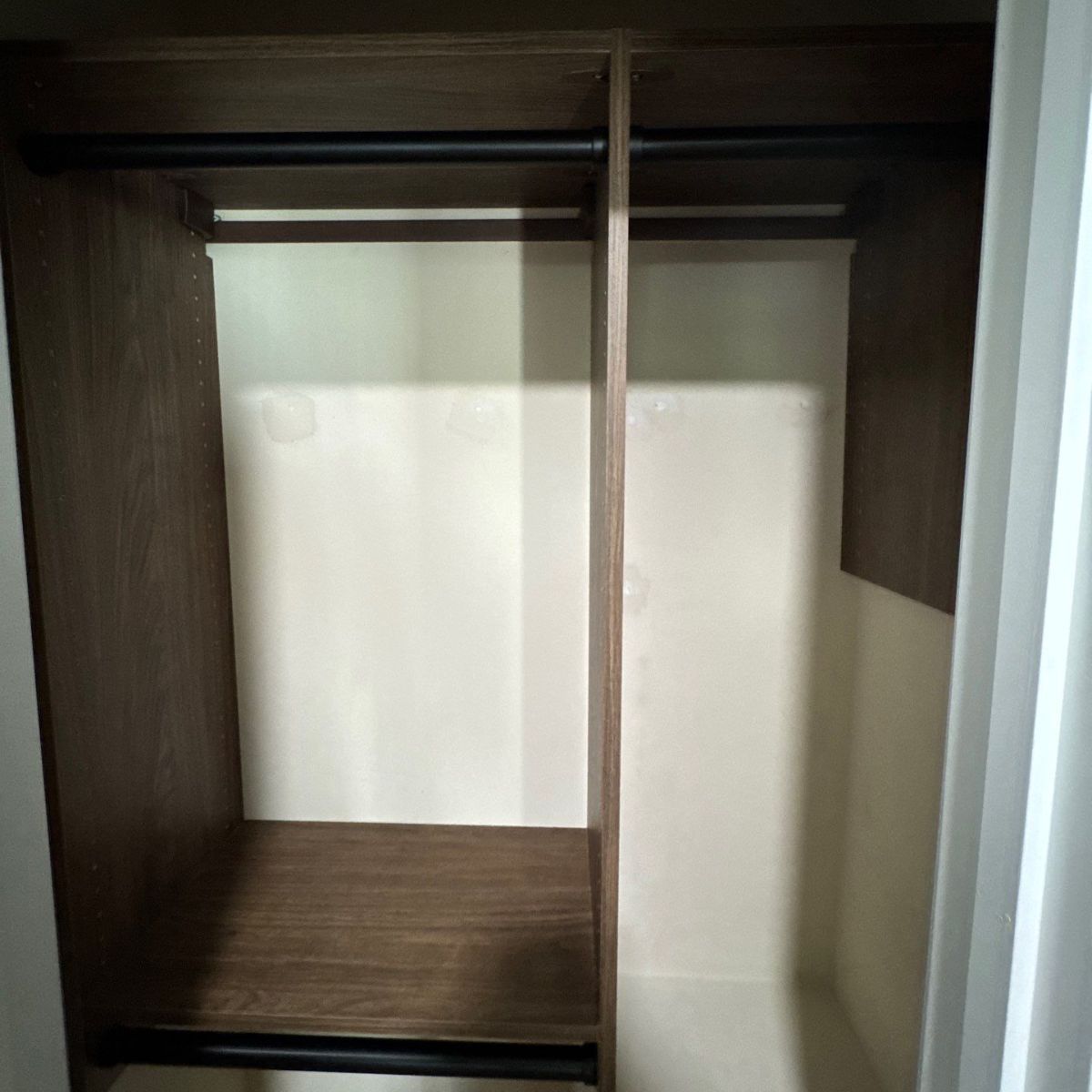 Empty closet with dark wood trim and a hanging rod. Ivory-colored walls and a divider create separate sections.