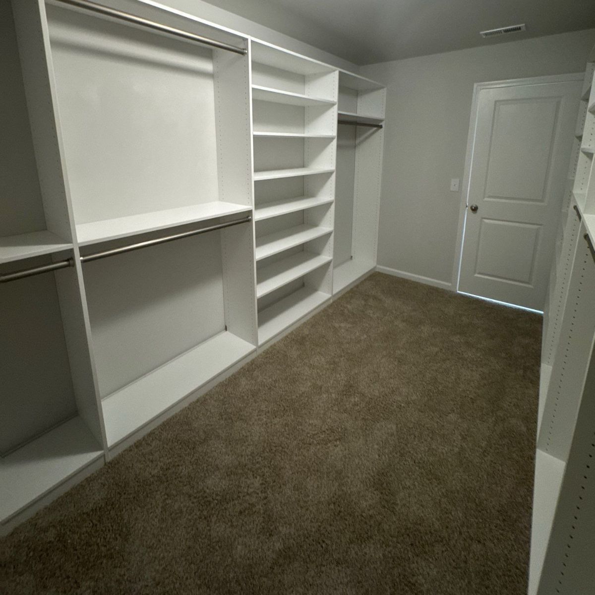 A white, organized closet with shelves and hanging rods, featuring a brown carpet and a white door.