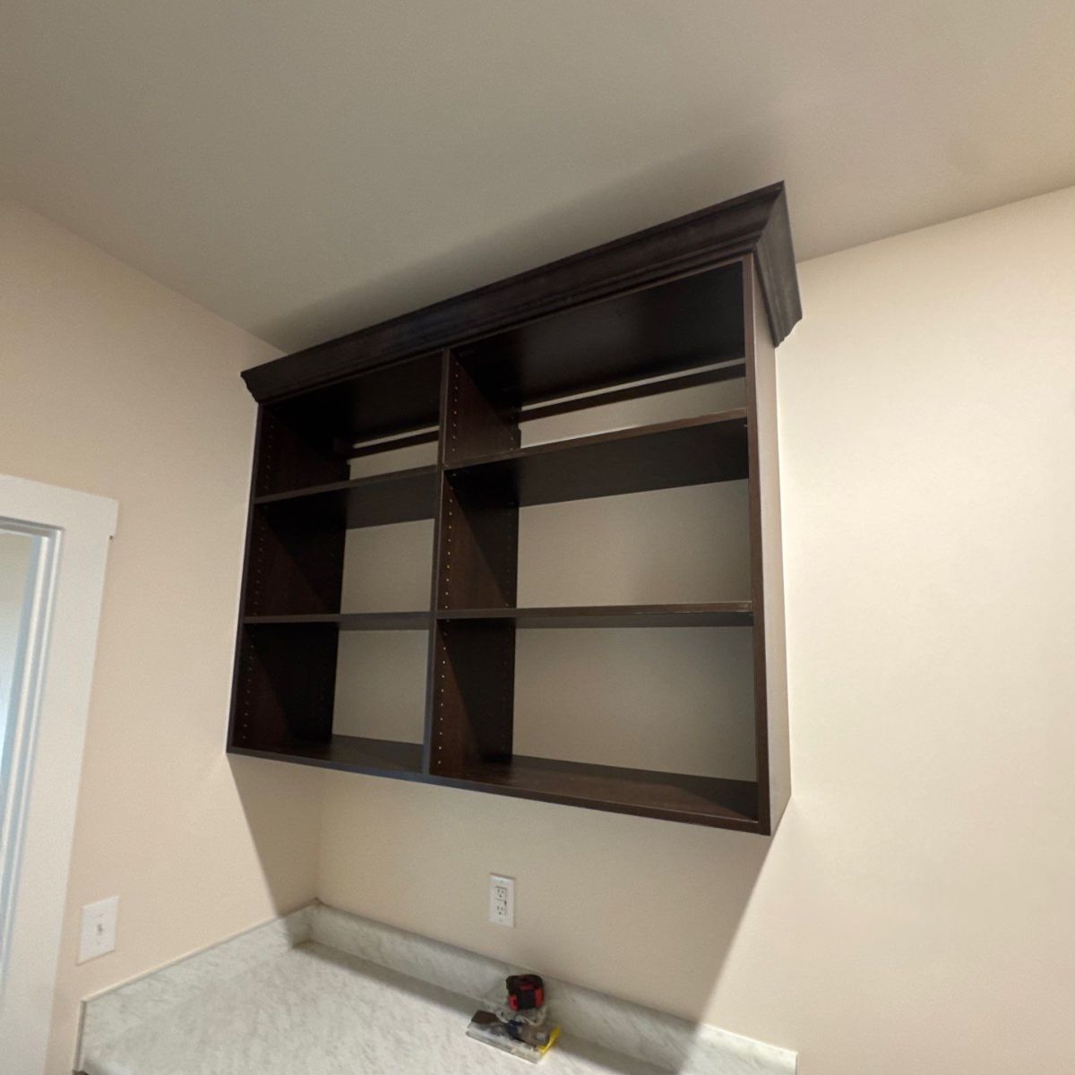 Dark brown wooden shelves mounted on a light beige wall above a countertop.