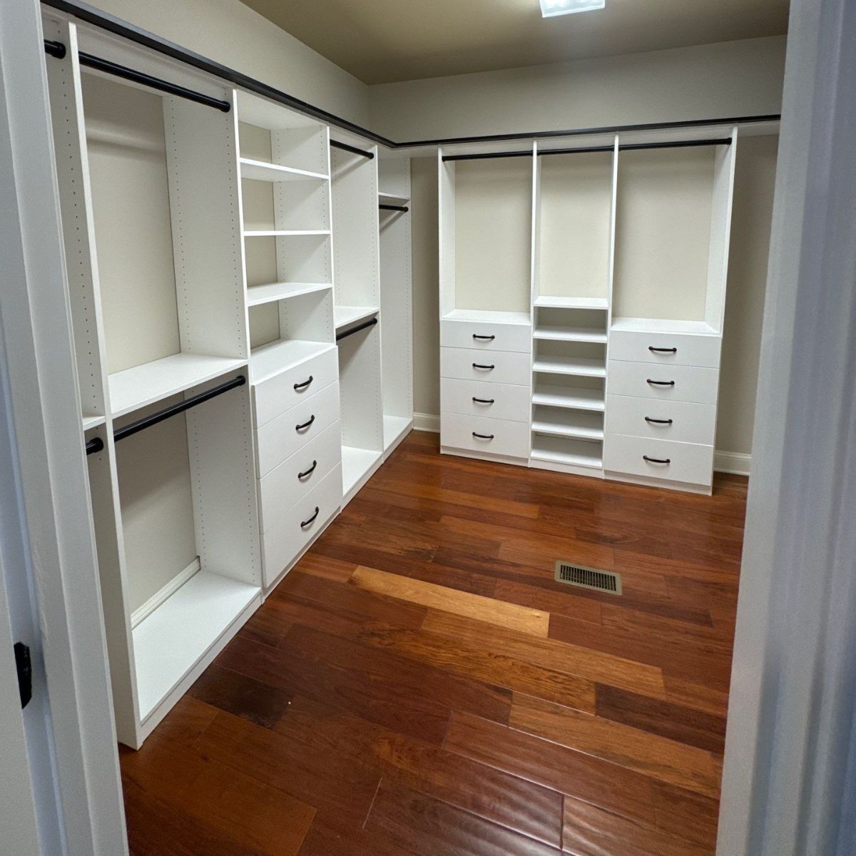 Empty white walk-in closet with built-in shelves, drawers, and hanging rods; hardwood floors.