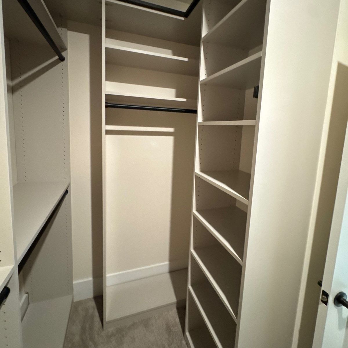 Empty walk-in closet with white shelves and hanging rods. The walls are painted a light neutral color.