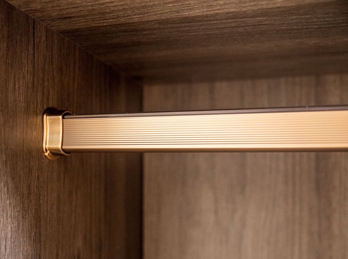 A close up of a brass clothes rack in a wooden wardrobe.