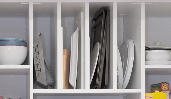 A kitchen shelf with plates , bowls , and utensils on it.