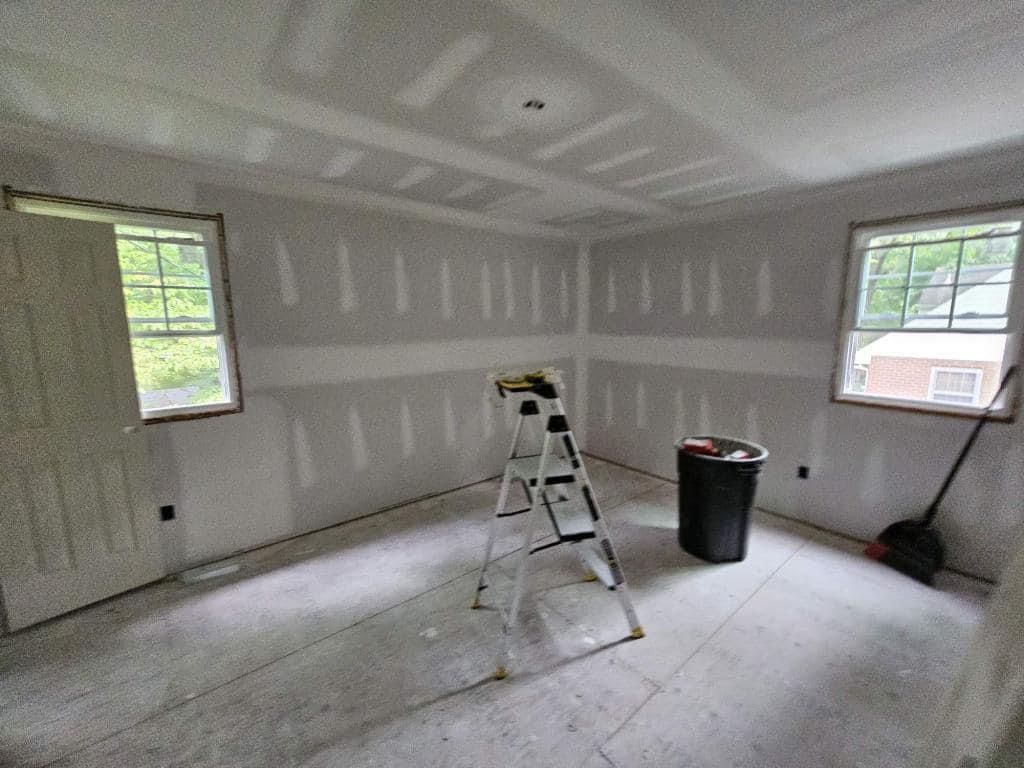 A room with a ladder and a trash can in it.