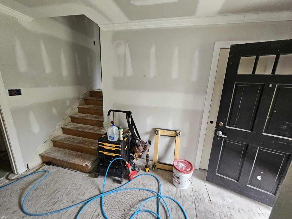 A room with stairs , a door and a hose in it.