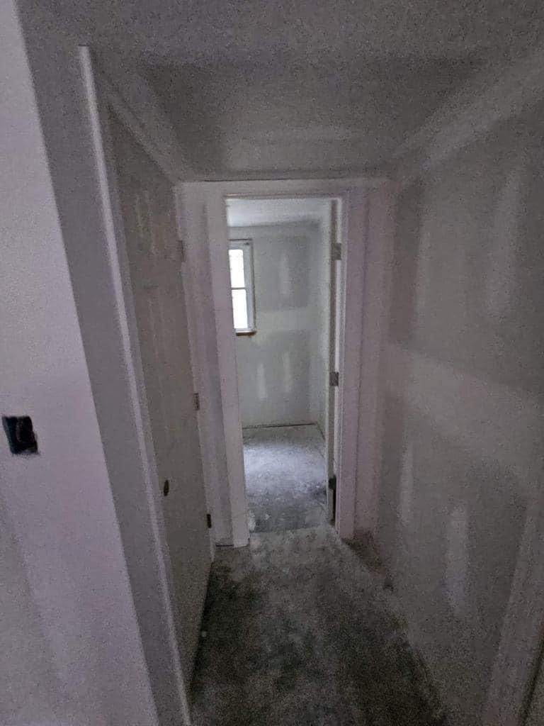 A hallway with drywall on the walls and a door leading to a room.