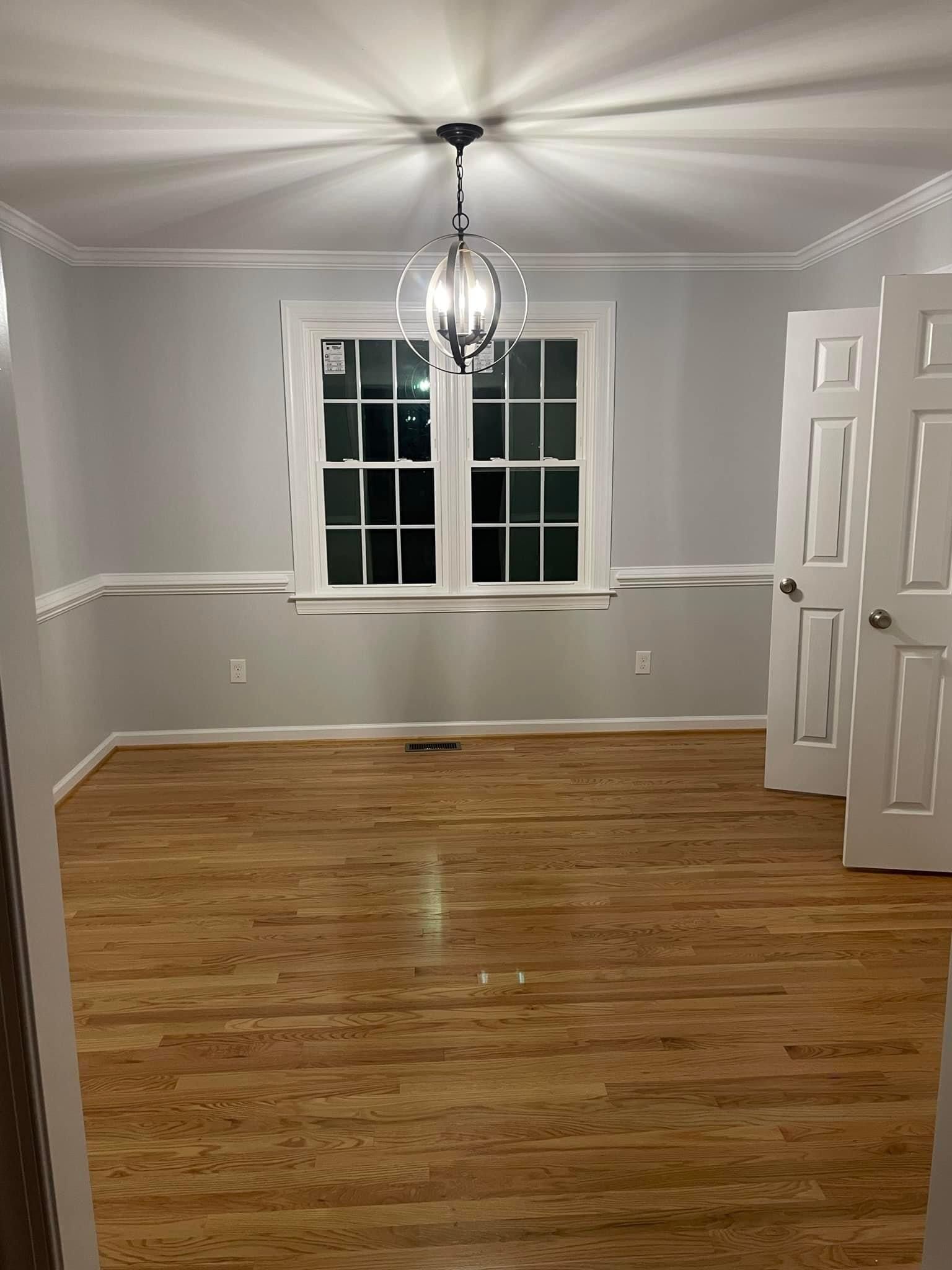 An empty dining room with hardwood floors and a chandelier hanging from the ceiling.