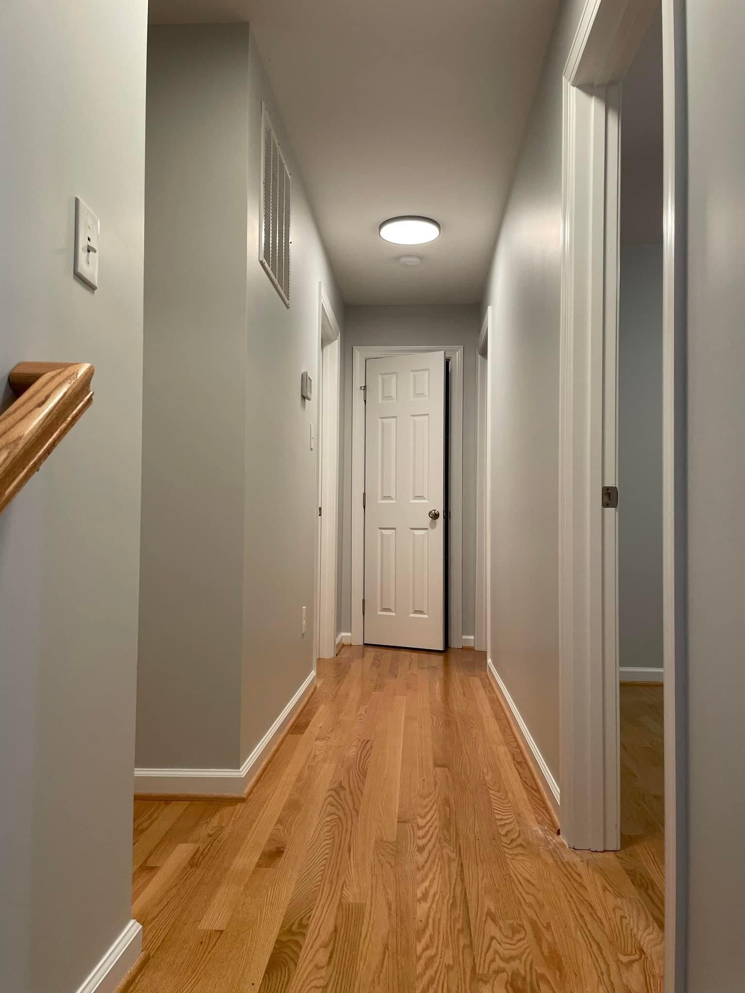 A long hallway with hardwood floors and white walls in a house.