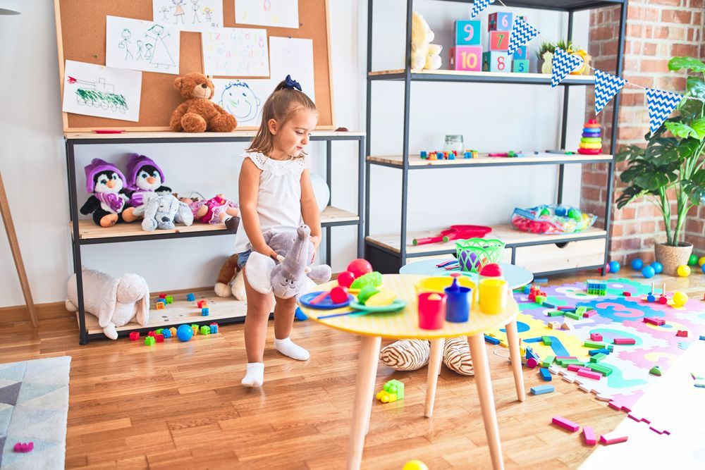 A little girl is playing with toys in a messy room.