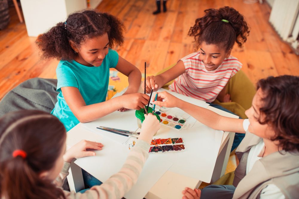 A group of children are sitting around a table painting.