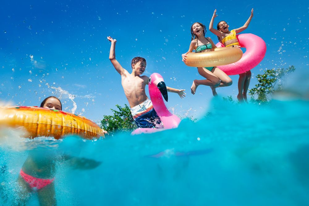 A group of people are jumping into a swimming pool with floats.