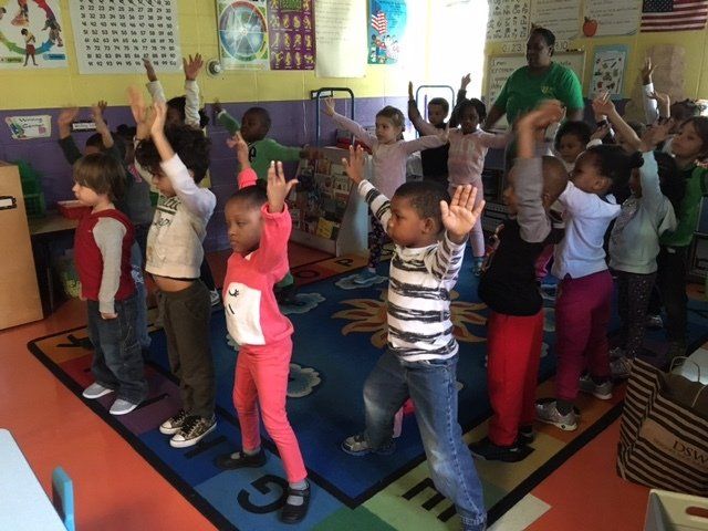 A group of children are standing on a rug with the letter g on it