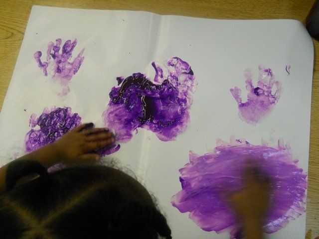 A child is making purple handprints on a piece of paper