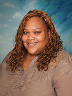 A woman with curly hair is smiling and wearing a brown shirt.