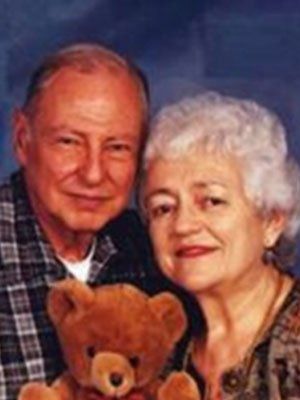 A man and woman are posing for a picture with a teddy bear
