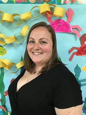 A woman in a black shirt is smiling in front of a wall with paper crabs on it.