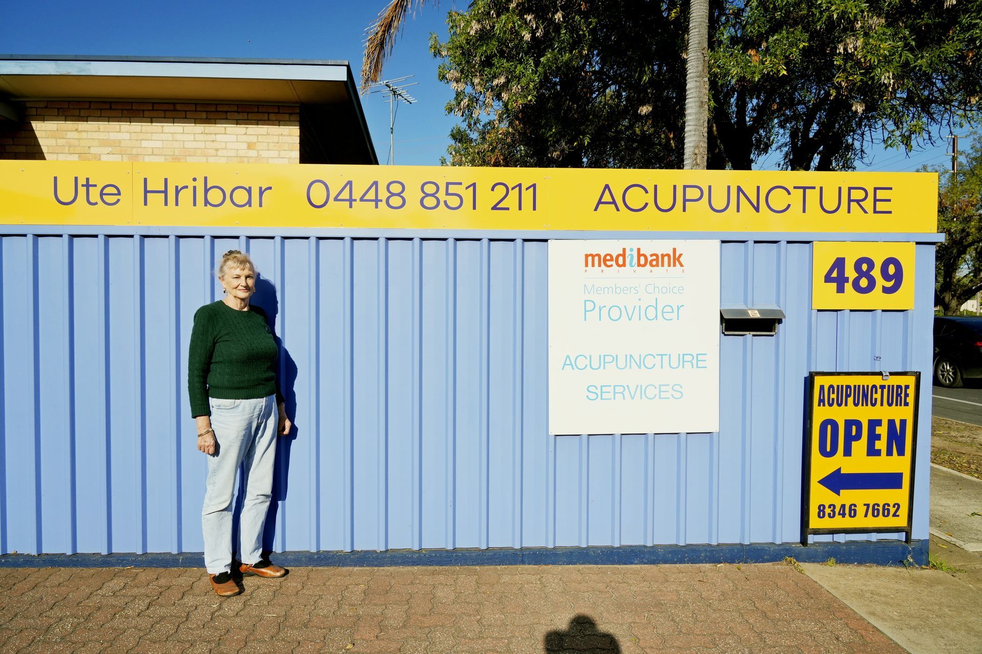 Exterior of acupuncture clinic; blue corrugated fence with signs and an open sign.