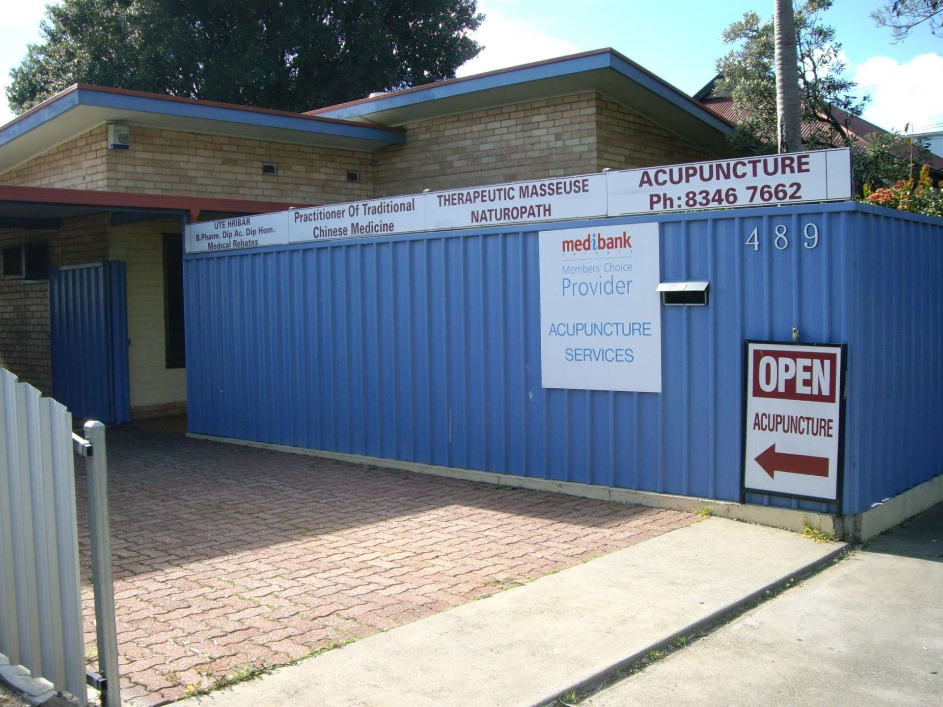 Exterior of acupuncture clinic; blue corrugated fence with signs and an open sign.