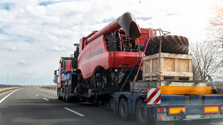 Red combine harvester transported on a flatbed trailer on a highway.