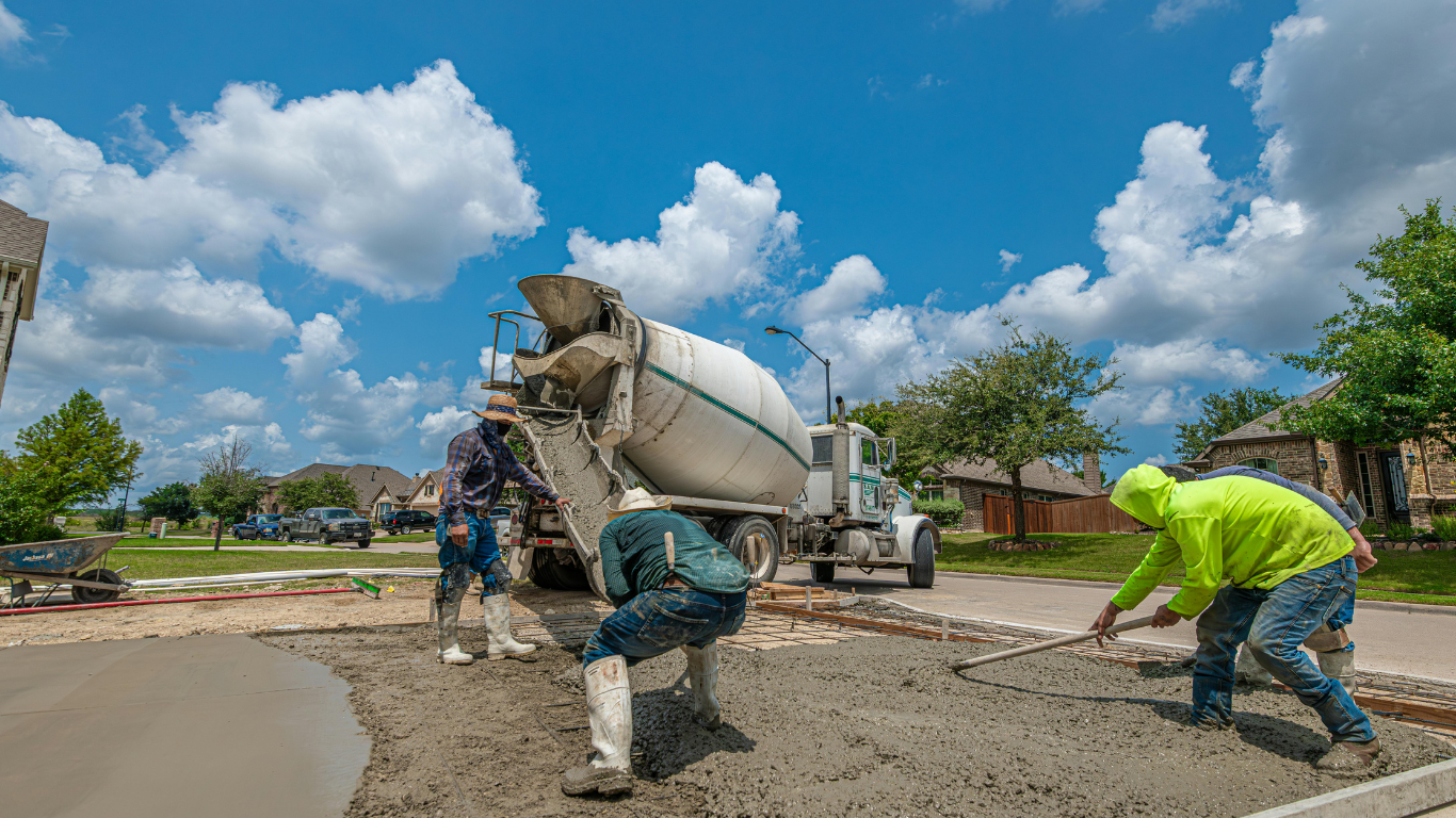 Workers pouring concrete from a mixer truck onto a driveway on a sunny day.