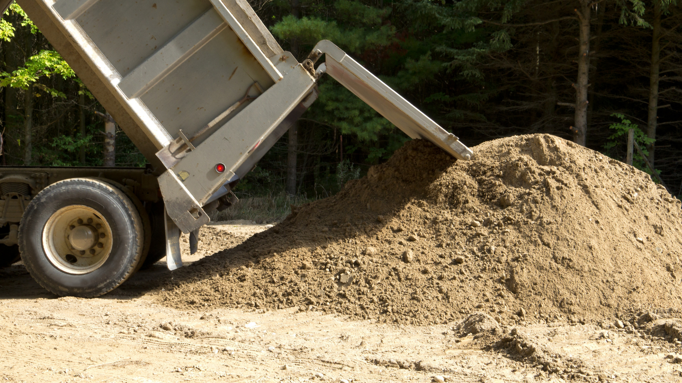 Dump truck unloading a pile of brown soil.