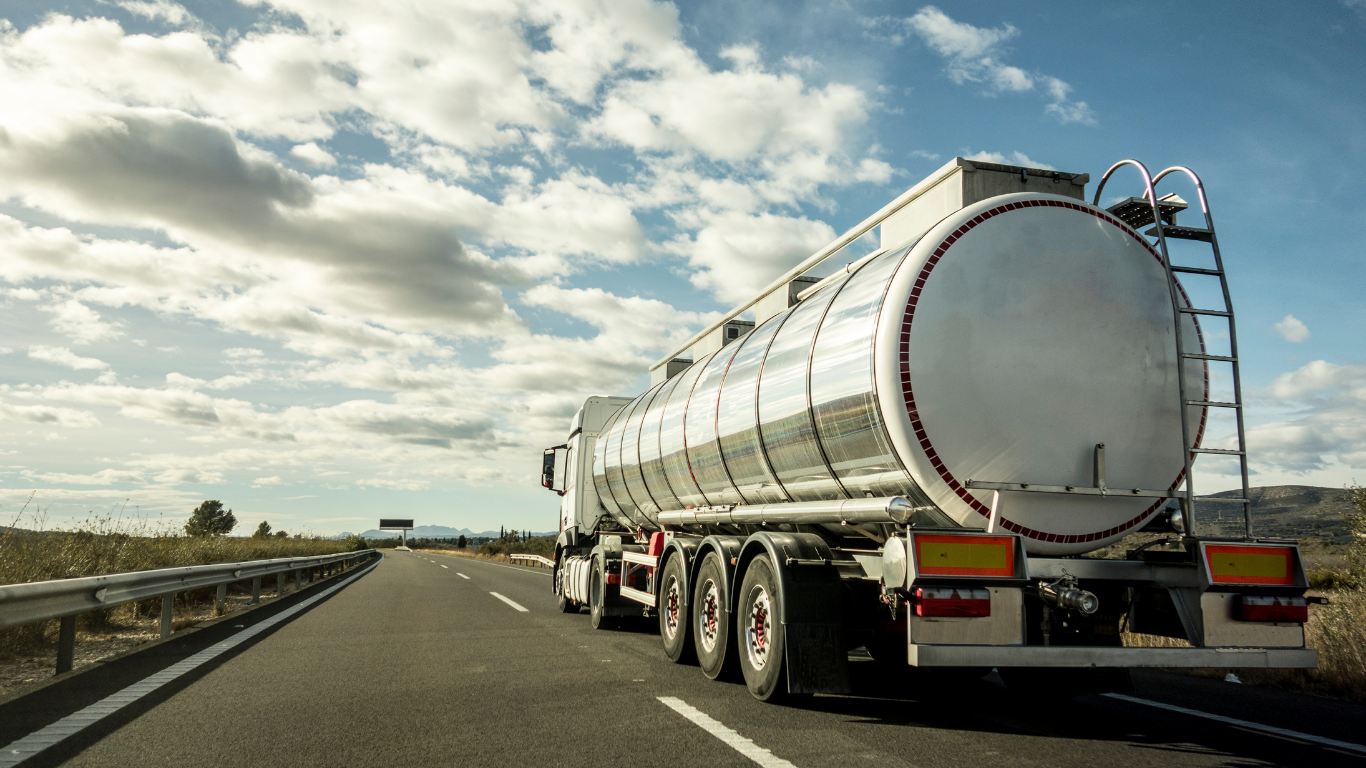 Tanker truck driving down a highway on a sunny day with a cloudy sky.