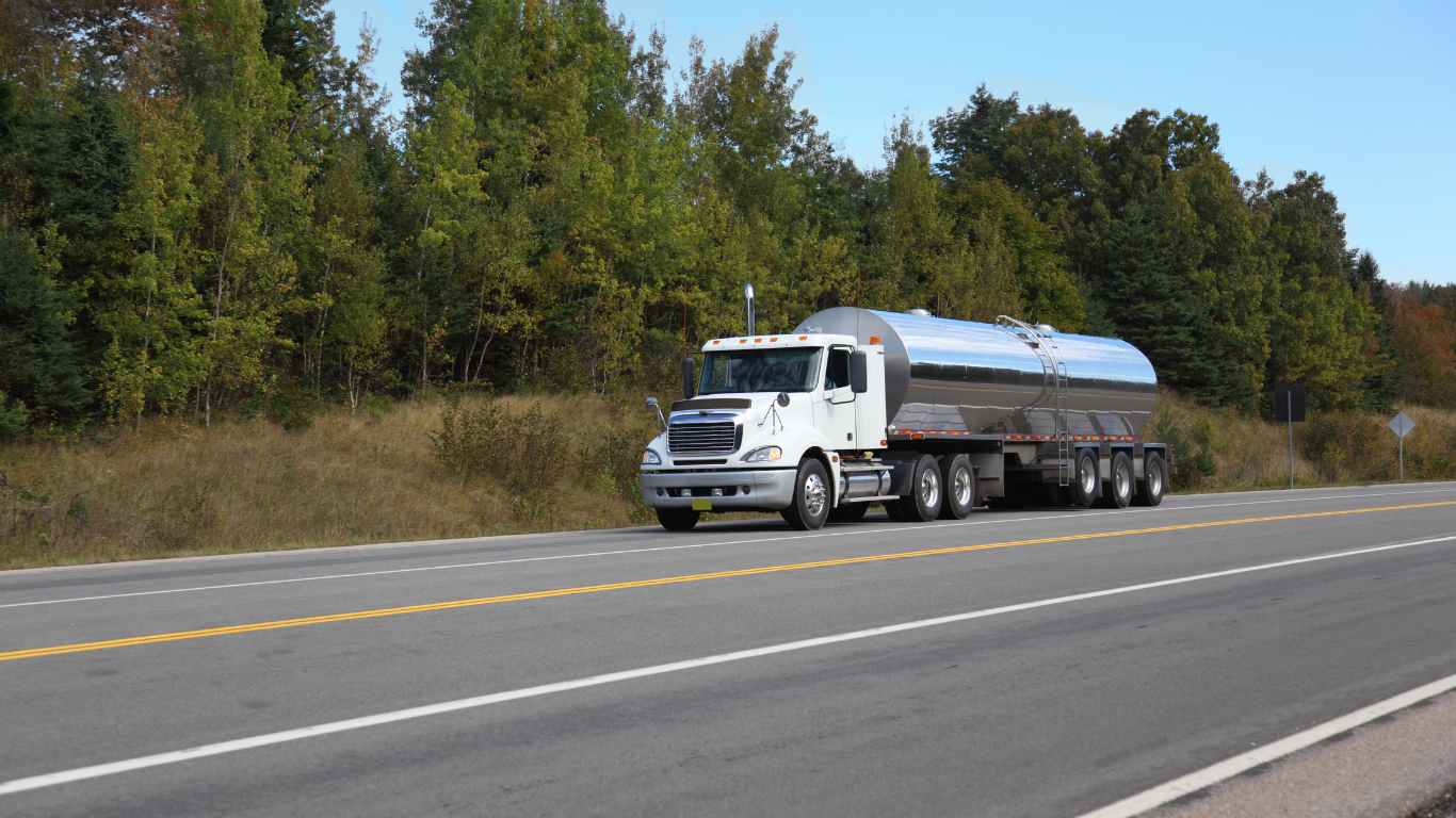 Tanker truck driving on a two-lane road, trees in the background.